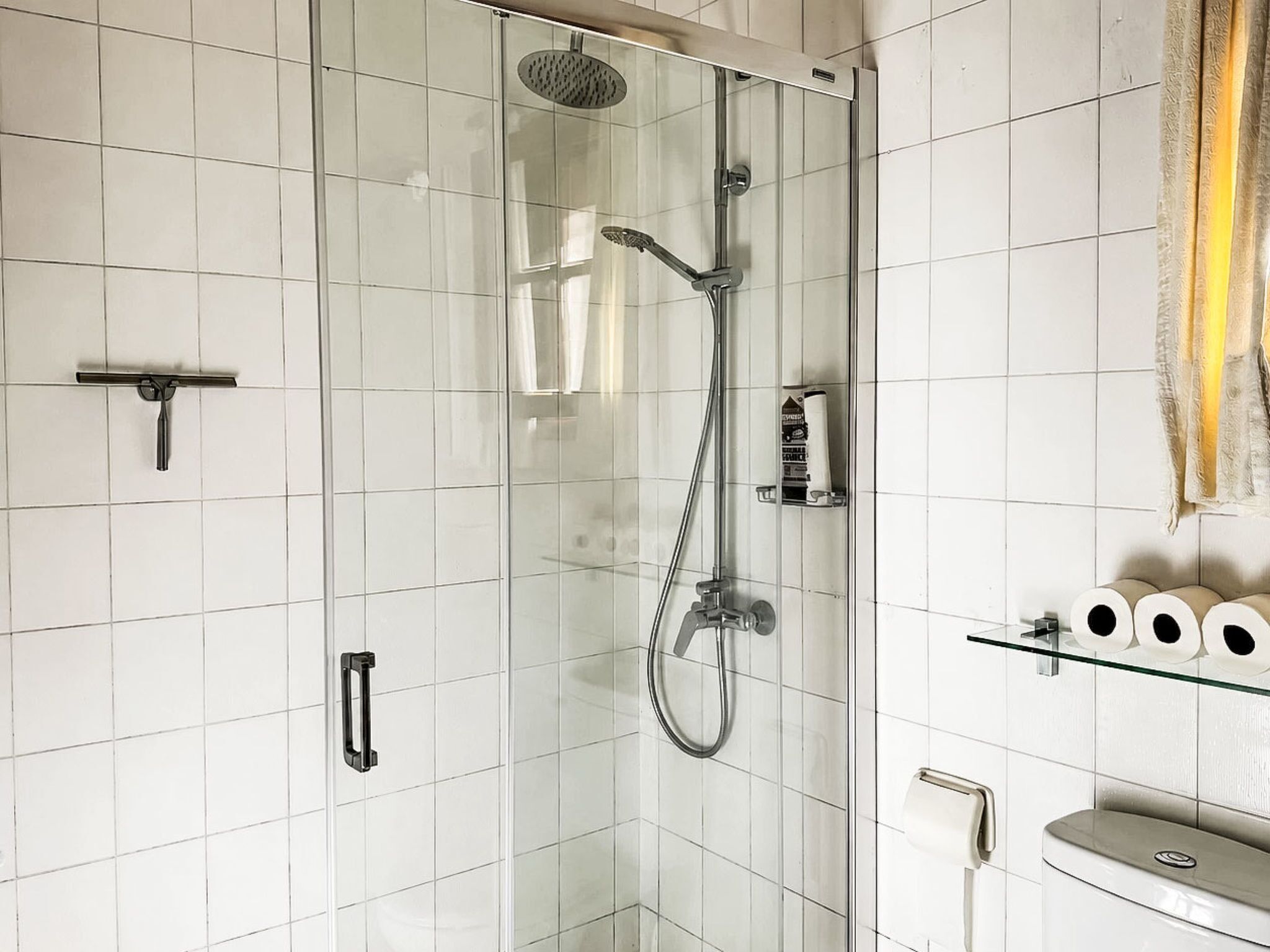 Een moderne badkamer met een douchecabine van glas, een toiletrolhouder en een glazen plank met toiletpapier.