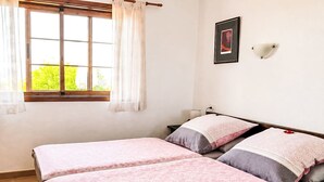Een slaapkamer met twee bedden, een raam met gordijnen, een wandlamp en een lijst met een afbeelding.