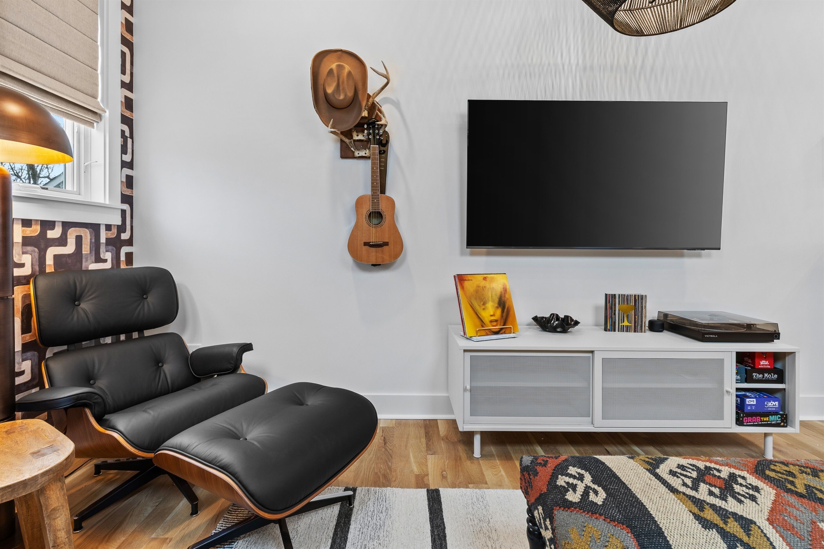 A modern living room with a black leather sofa, a mounted guitar, a TV, and a white entertainment unit with records.