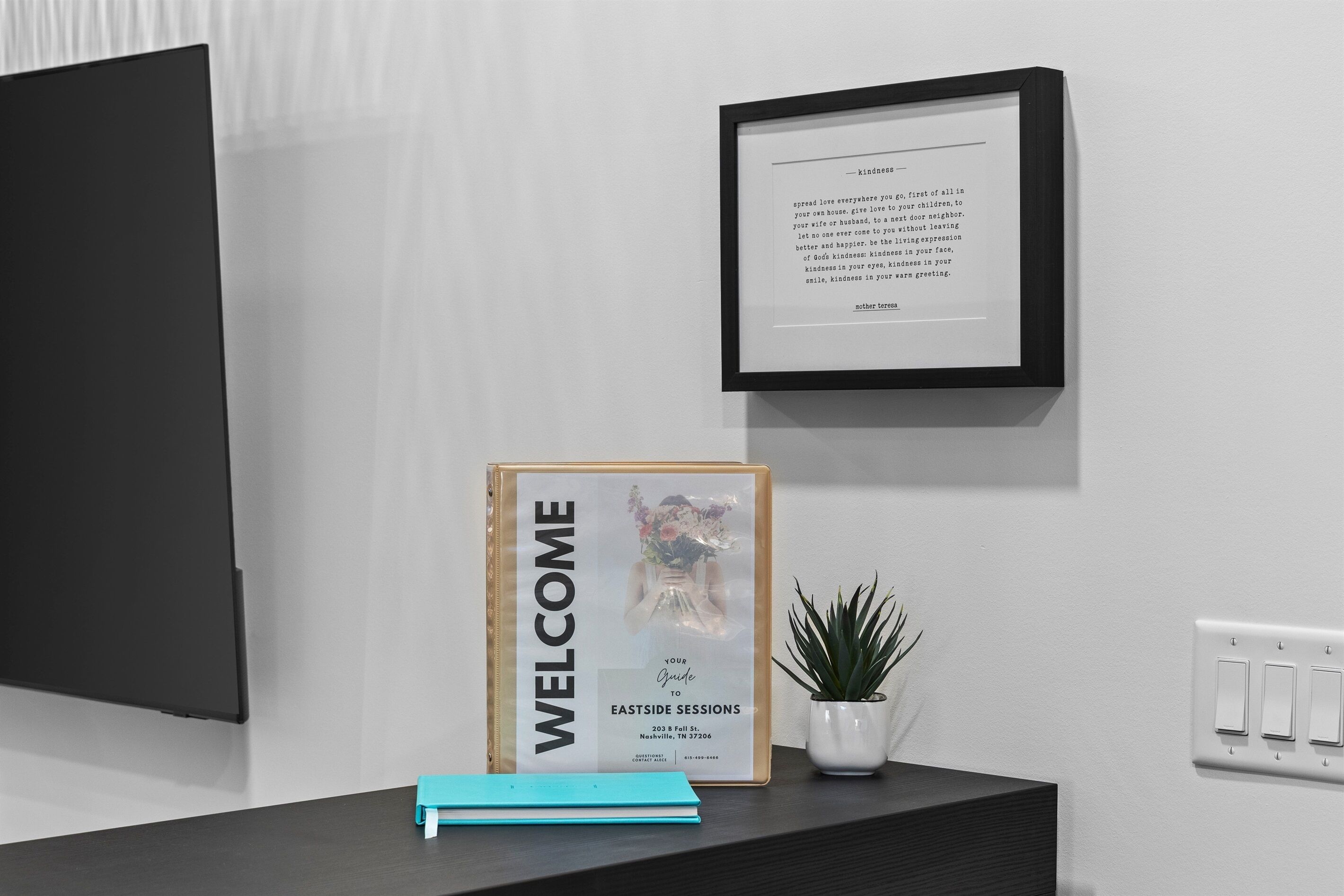 A framed welcome sign, a framed guide to Eastside Sessions, and a small potted plant on a desk.