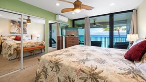 A bedroom with a bed, a bench, a dresser, a television, and a balcony with a view of the ocean. - New Listing! Stunning Oceanfront Sunsets (Lahaina)