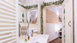 Ein Badezimmer mit weißem Waschbecken, einem Spiegel und einer Heizung. An der Wand steht eine Pflanze und die Tür ist mit einem Blattmuster verziert.