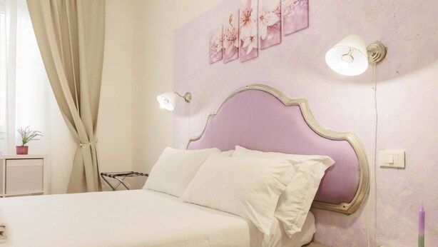 Ein Schlafzimmer mit einem Bett, einem Nachttisch, einer Lampe und einer Wand mit floralen Bildern.