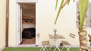 Eine geöffnete Tür, die in einen Raum führt, mit einem Sofa, einem kleinen Tisch mit einer Vase und einem Fenster mit Blick auf ein Gebäude.