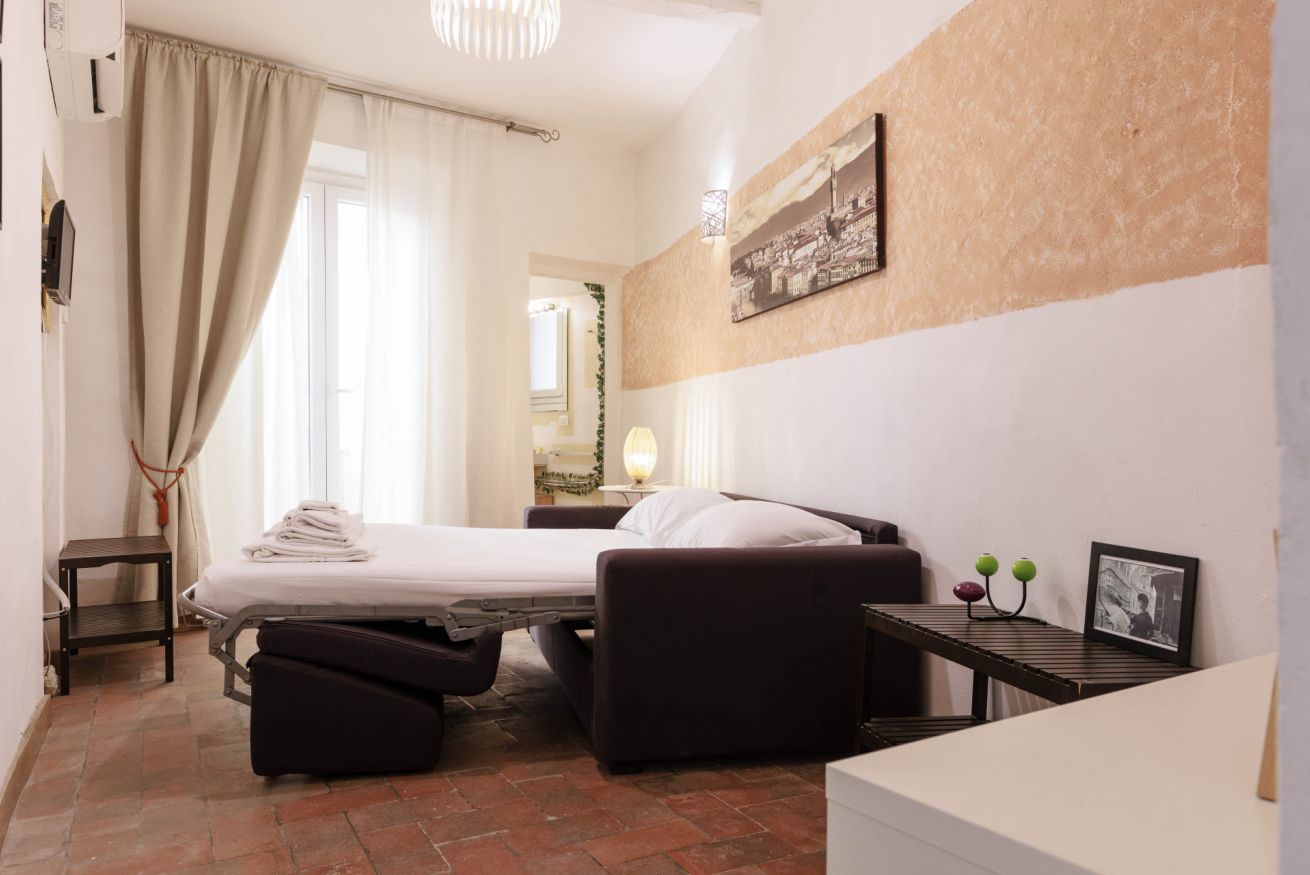 Una habitación de hotel pequeña con cama, una mesita, una silla y una maleta.