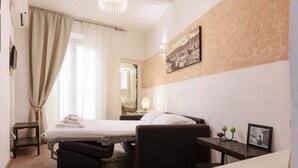 Ein kleines Hotelzimmer mit Bett, Tisch, Stuhl und Koffer.