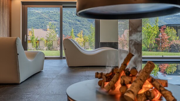 Een moderne kamer met een open haard, een witte bank en uitzicht op een bergachtig landschap door grote ramen.