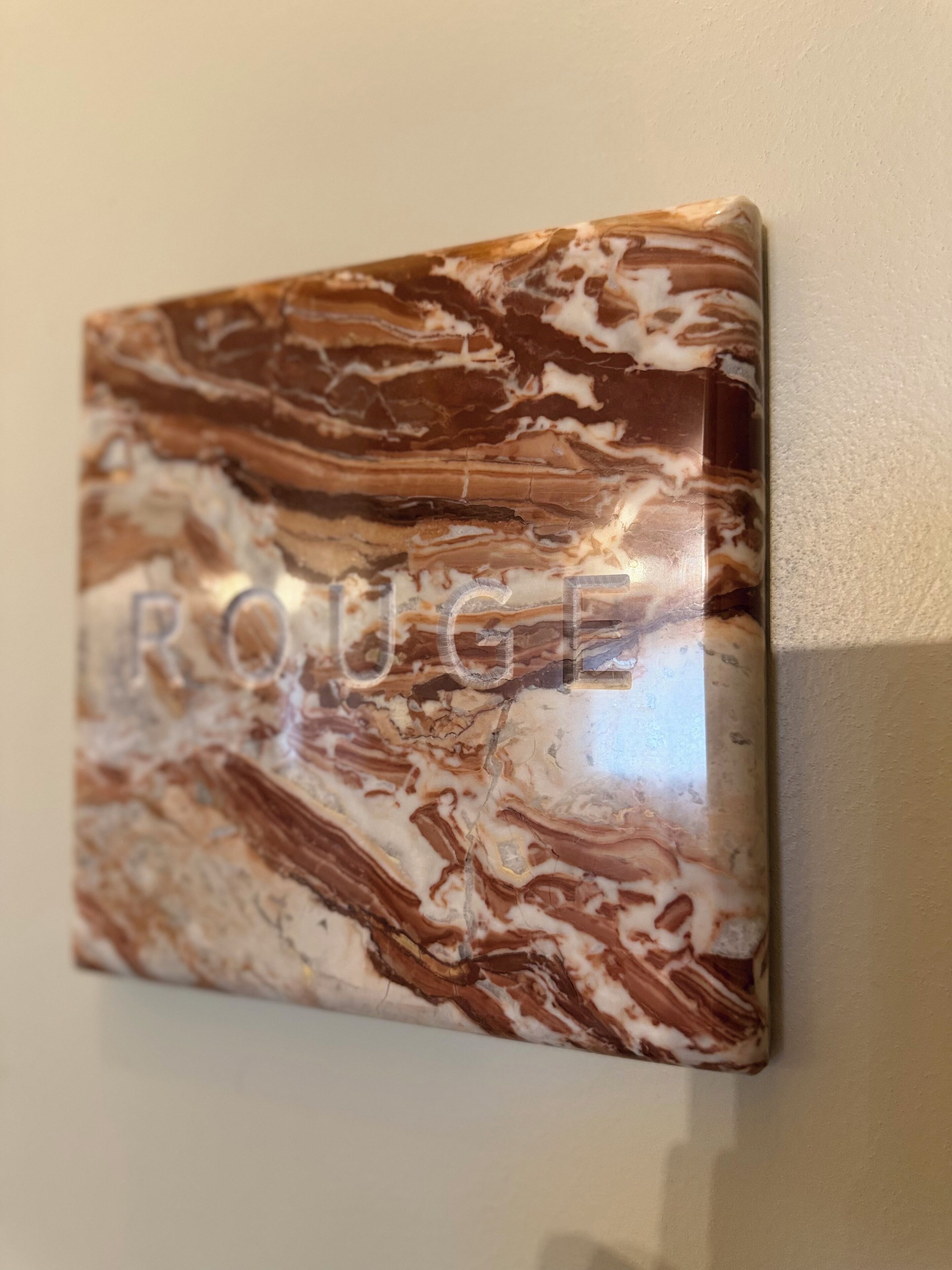 A marble wall art piece with the word "ROUGE" on it.