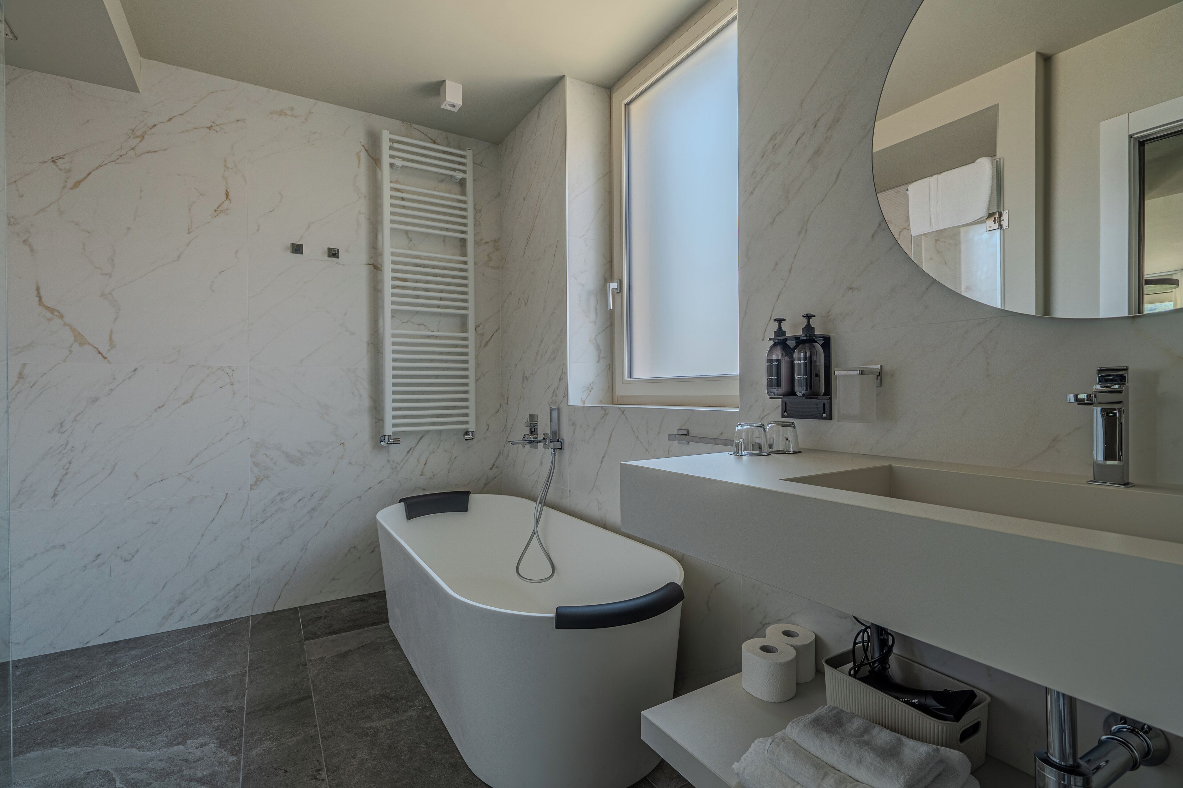Un baño moderno con una bañera independiente, un tocador con espejo y una ventana que proporciona luz natural.