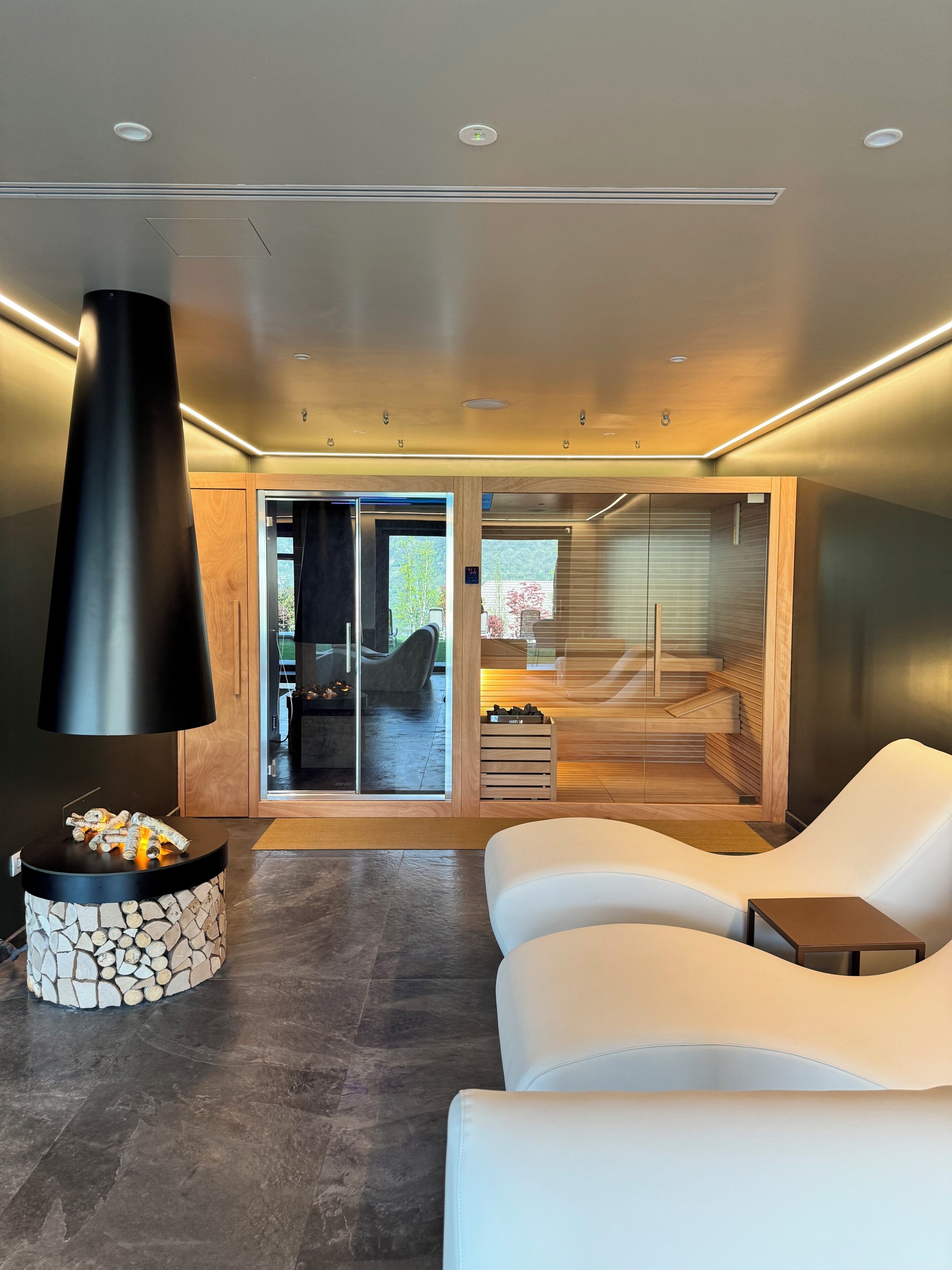 Un intérieur moderne avec une cheminée, un canapé en cuir blanc et une vue sur un sauna en bois.