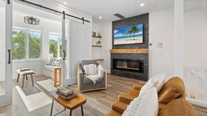 A modern living room with a fireplace, a large window, and a cozy seating area. - Beautifully Decorated 2 BR Townhome - Cedars East #802 by RVA (Longboat Key)