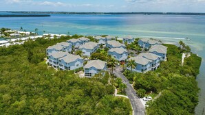 A resort with multiple blue buildings surrounded by lush greenery and a clear view of the ocean. - Beautifully Decorated 2 BR Townhome - Cedars East #802 by RVA (Longboat Key)