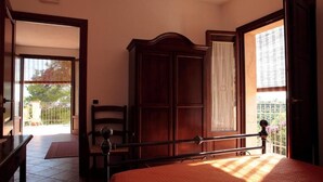 Een slaapkamer met een bed, een kledingkast, een stoel en een bureau. Er is een raam met gordijnen en uitzicht op het omliggende landschap.