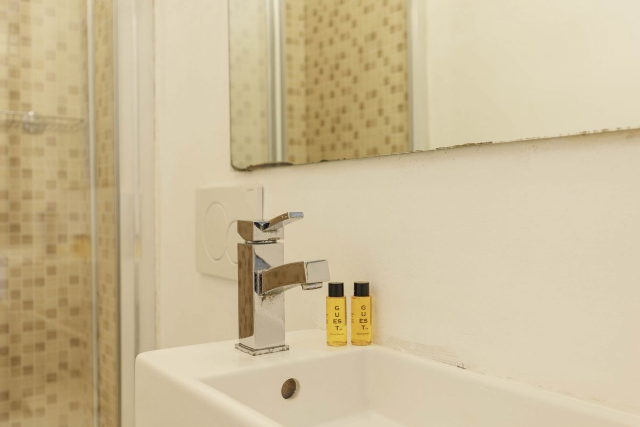 Une salle de bain avec un lavabo blanc, un robinet chromé et deux bouteilles jaunes étiquetées « POUR LES INVITÉS ».