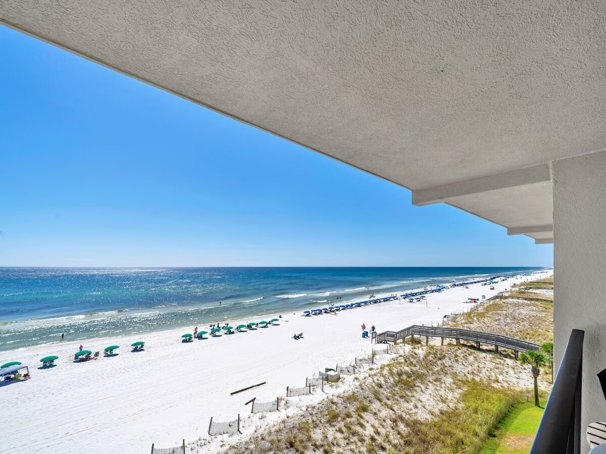 A beach view from a balcony with a clear sky, sandy beach, and umbrellas.
