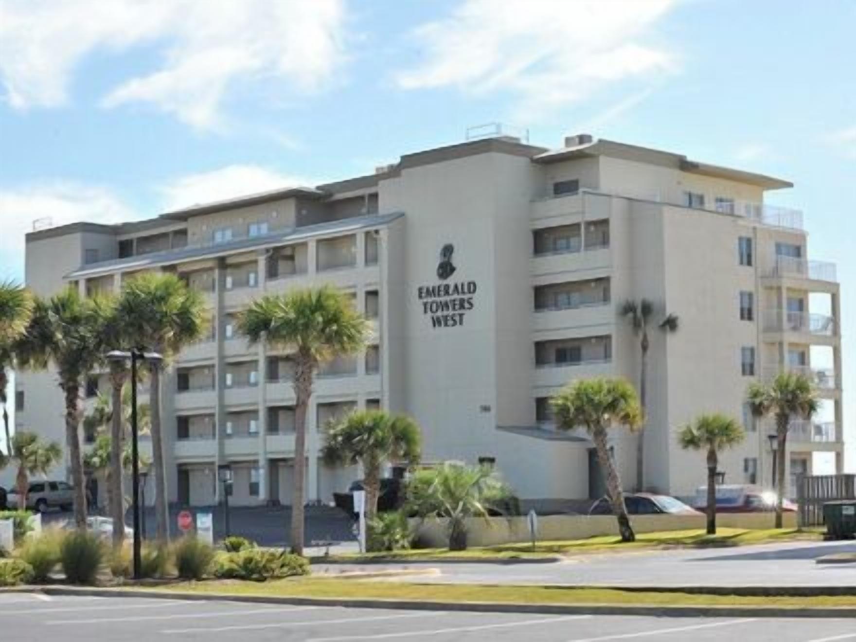 A multi-story hotel named Emerald Towers West with a modern architectural design, featuring balconies and a parking area in front.