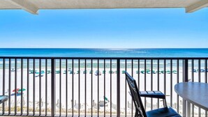 Un balcón con vista a la playa, que incluye barandilla, una mesa y una silla.