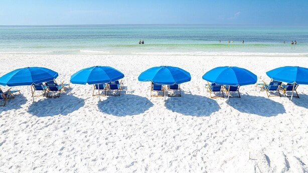 A beach with white sand and clear blue water. There are five blue umbrellas and matching beach chairs arranged in a row. - Top Floor Beachfront - Great Views From Top Floor! Beach Service! (Fort Walton Beach)