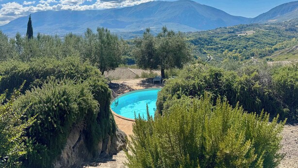 Una piscina rodeada de vegetación exuberante y montañas al fondo.