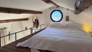 Un dormitorio con una cama grande, vigas de madera, un ventanal circular y una cabeza de ciervo montada en la pared.
