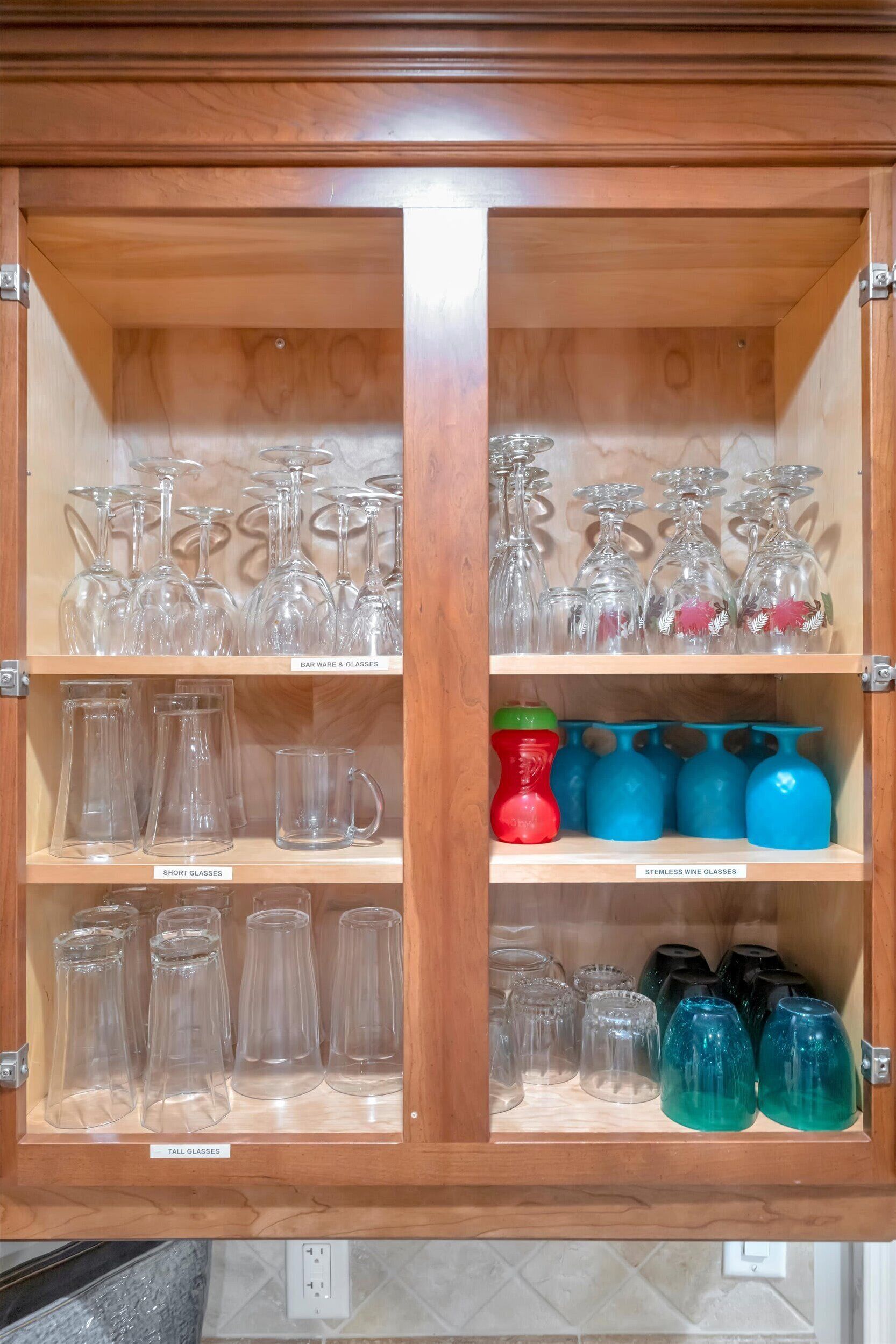 A wooden cabinet with shelves containing various glassware, including wine glasses, short glasses, and tall glasses.