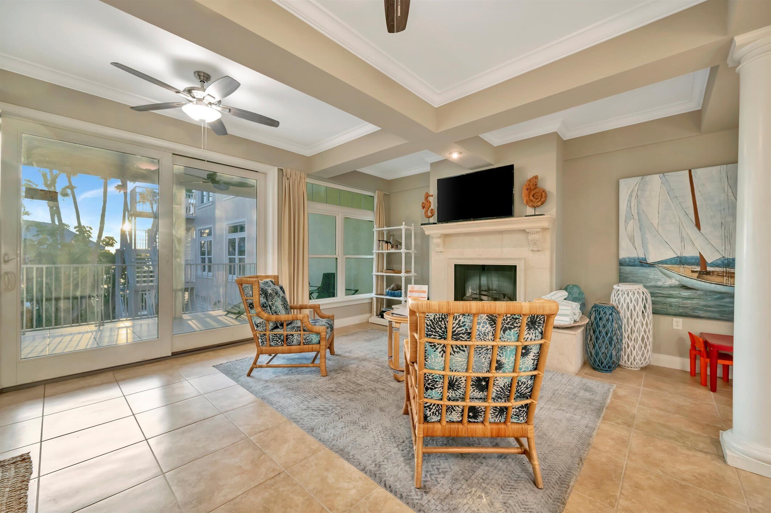 A spacious living room with a fireplace, large windows, and a ceiling fan.