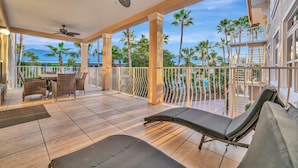 Un espacio al aire libre techado con comedor, sillas de descanso y vistas a palmeras y una piscina.