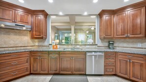 Cocina moderna con armarios de madera, encimeras de granito, lavavajillas de acero inoxidable y una isla central con fregadero.