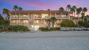 Un hotel frente a la playa con varios balcones, palmeras y una playa de arena.