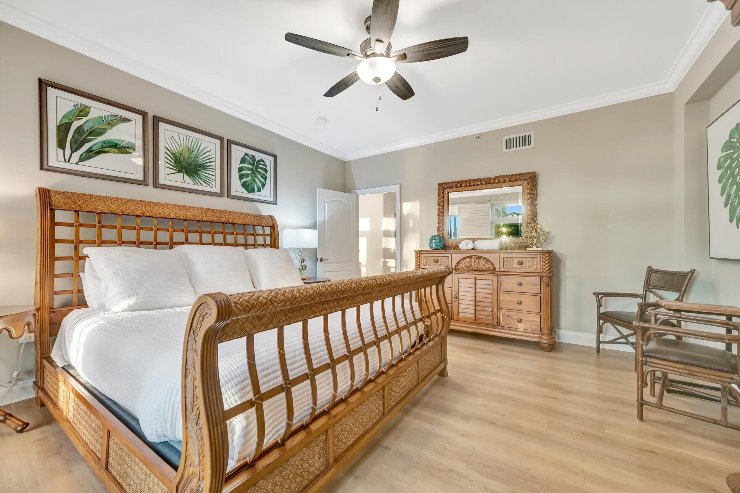 A bedroom with a wooden bed, a ceiling fan, a dresser, and framed botanical prints on the wall.