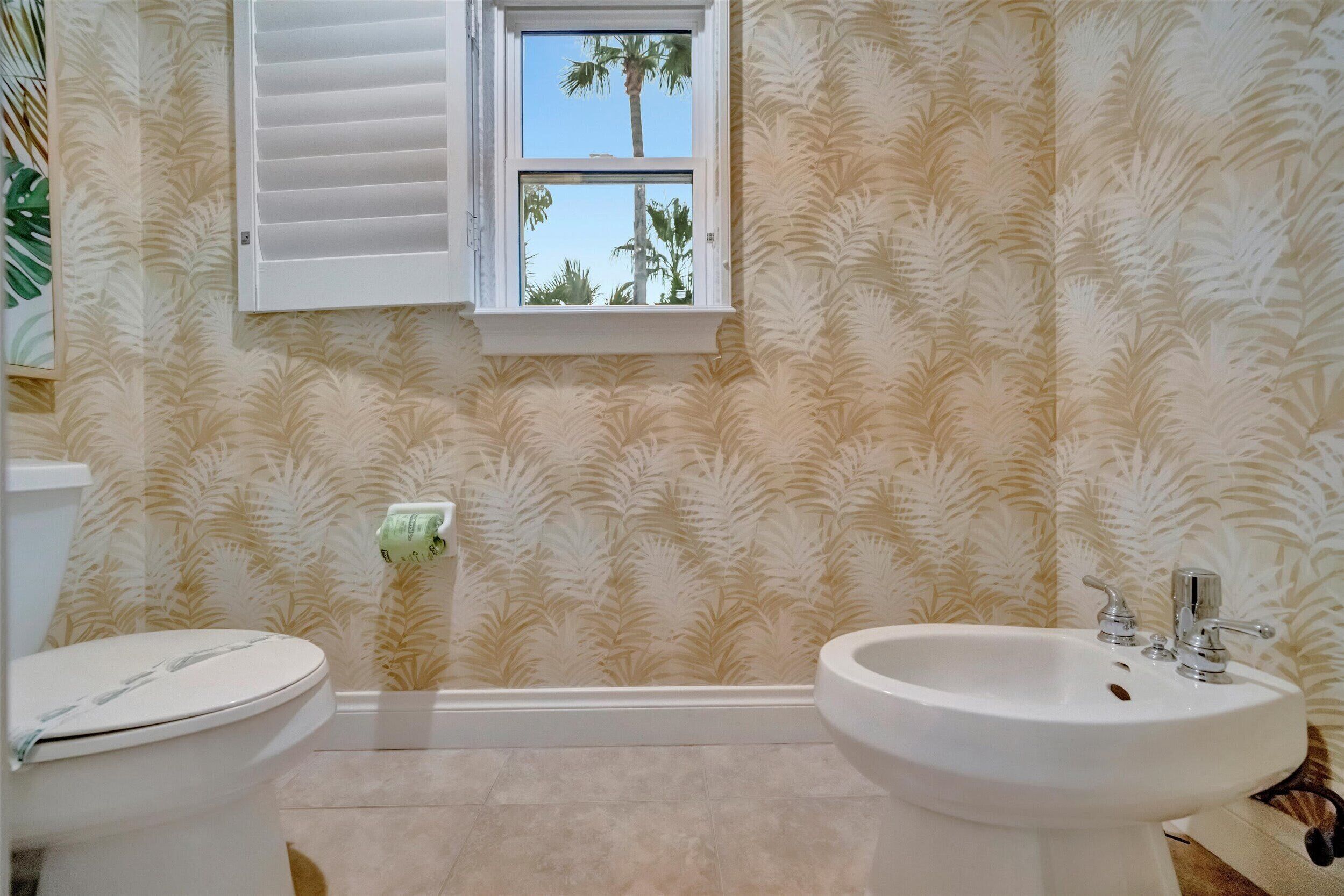 A bathroom with a toilet, sink, and window with palm trees outside.