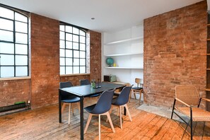 Una habitación con pared de ladrillo, un ventanal grande, una mesa con sillas y una estantería con un globo terráqueo y una botella.