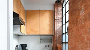 A compact kitchen with wooden cabinets, a washing machine, and a window with bars. - Spacious Studio in a Converted Warehouse Shoreditch (London)