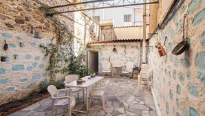 A stone-floored patio with white chairs and a table, surrounded by walls with blue patterns and a metal railing. - Mikos - Mansion in the City Center (Lesvos)