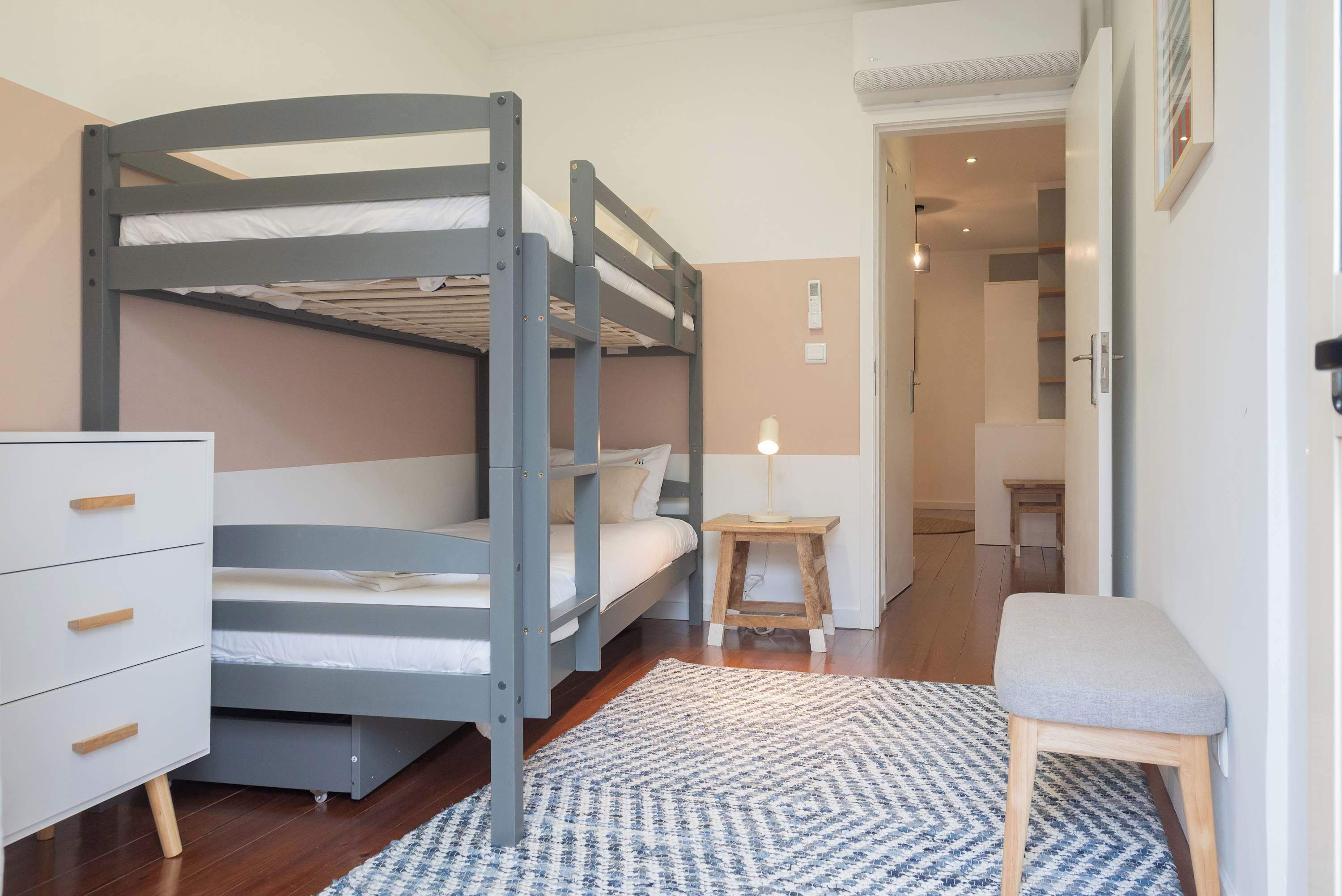 A bunk bed room with a wooden dresser, a small stool, and a patterned rug.