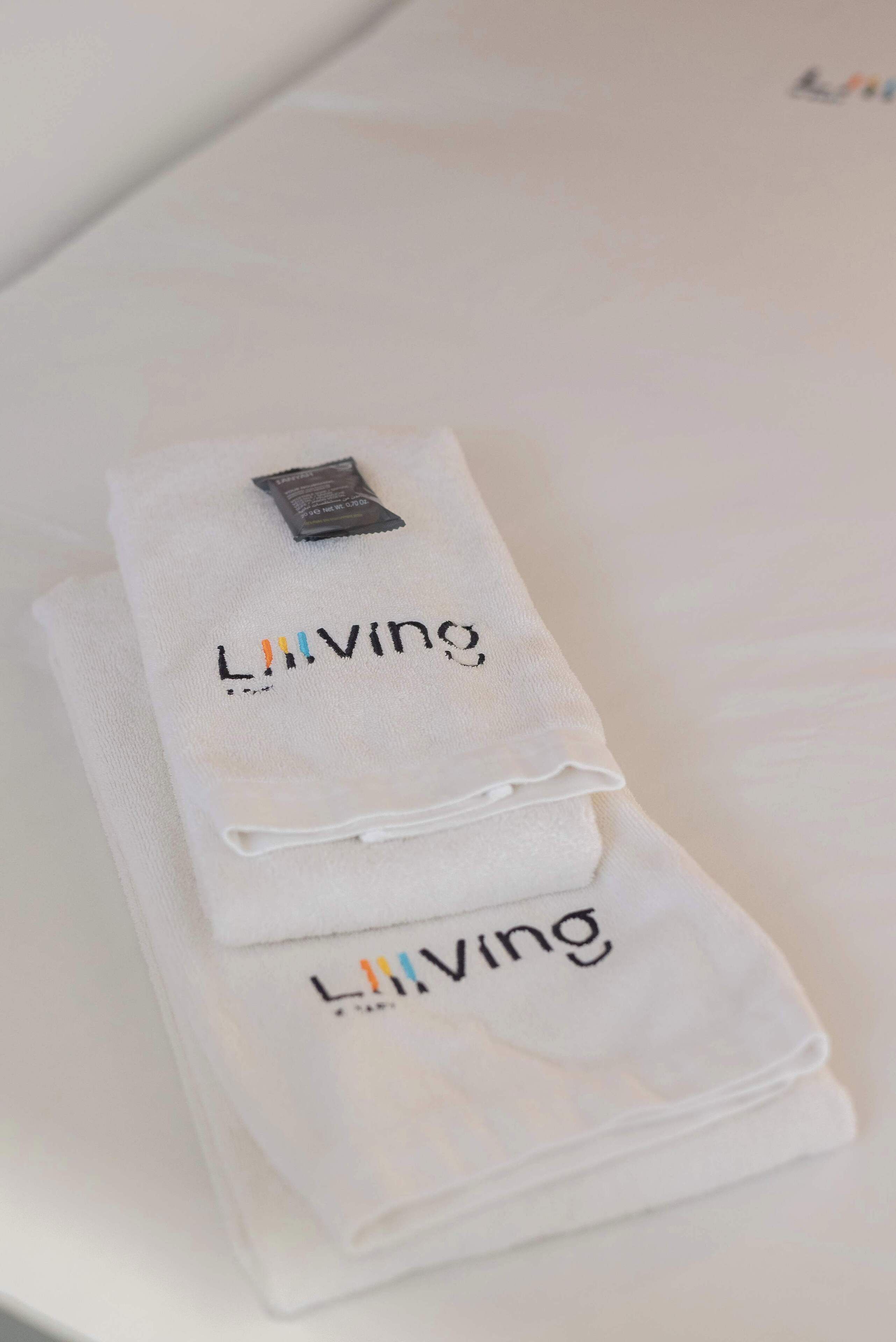 A neatly folded white towel with the word "Living" embroidered on it, placed on a white surface.