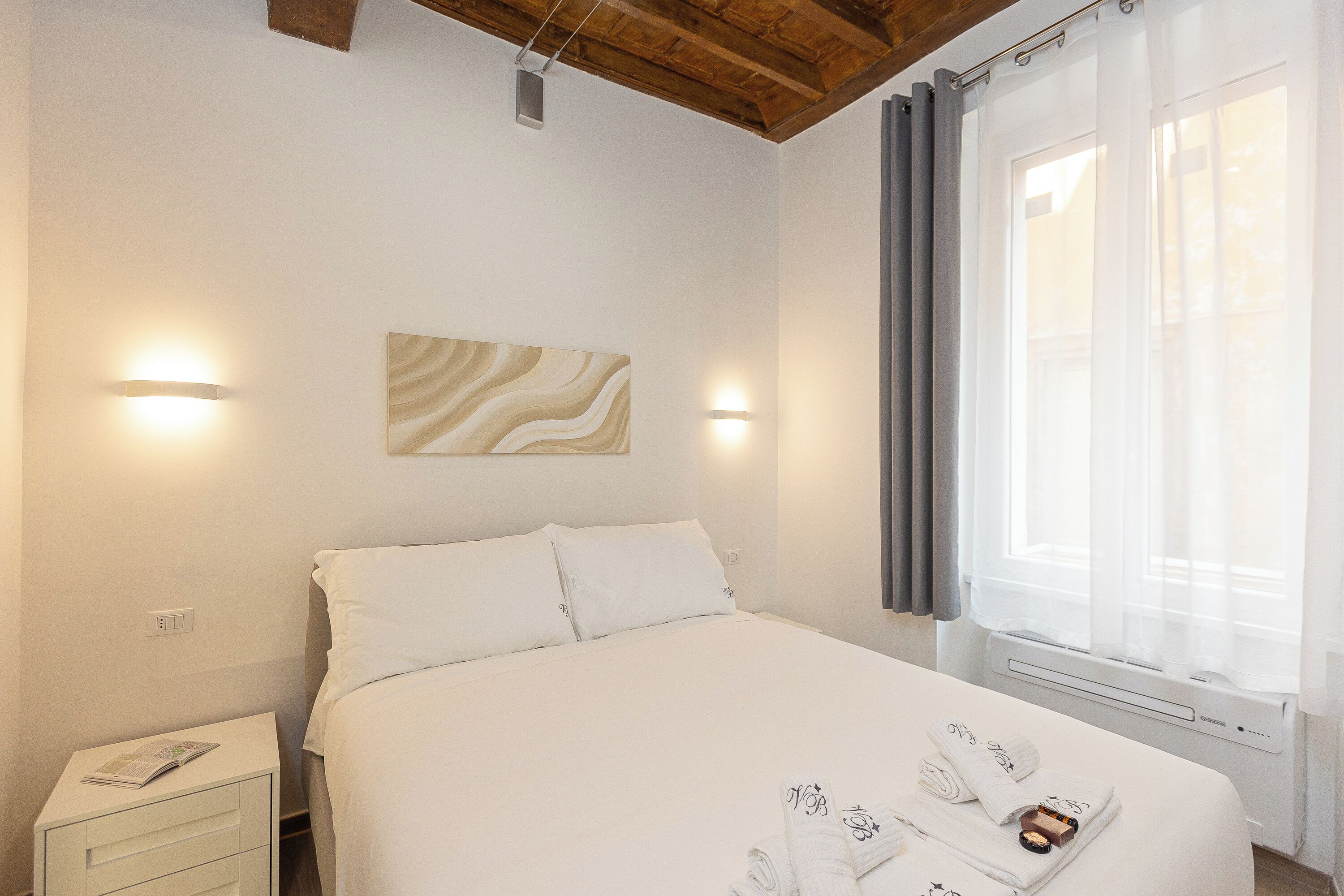 A clean, well-lit bedroom with a bed, bedside tables, and a window with curtains.