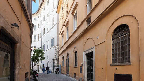 A narrow street with historic buildings, cobblestone pavement, and a few pedestrians. - Rental in Rome Navona Modern Apartment (Rome)