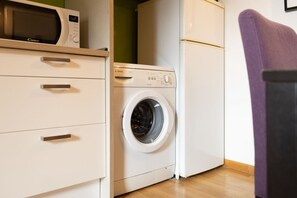 Ein kleiner Waschbereich mit Waschmaschine, Mikrowelle und Kühlschrank.