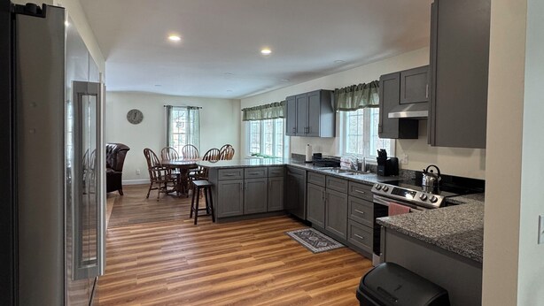 A modern kitchen with grey cabinets, a wooden dining table, and a black trash bin. - Amazing 3-bedroom home, Full Kitchen, in Newcastle perfect for your getaway (Newcastle)