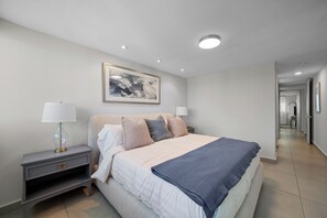 A modern bedroom with a large bed, bedside tables, a framed artwork, and a hallway leading to other rooms.