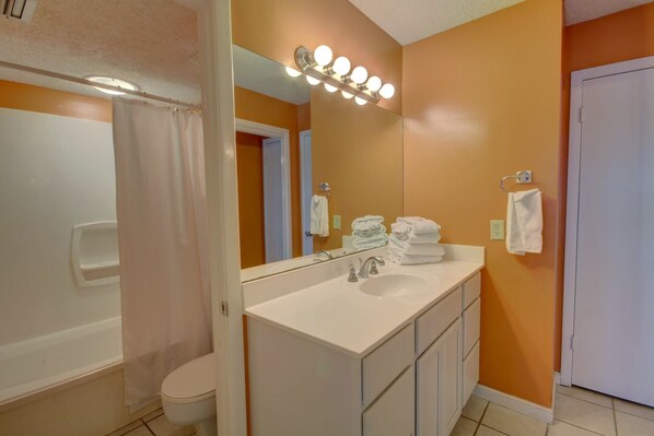A bathroom with a white sink, a mirror with lights, a shower curtain, and a toilet. - 459 El Matador 2 Bedroom Condo (Fort Walton Beach)