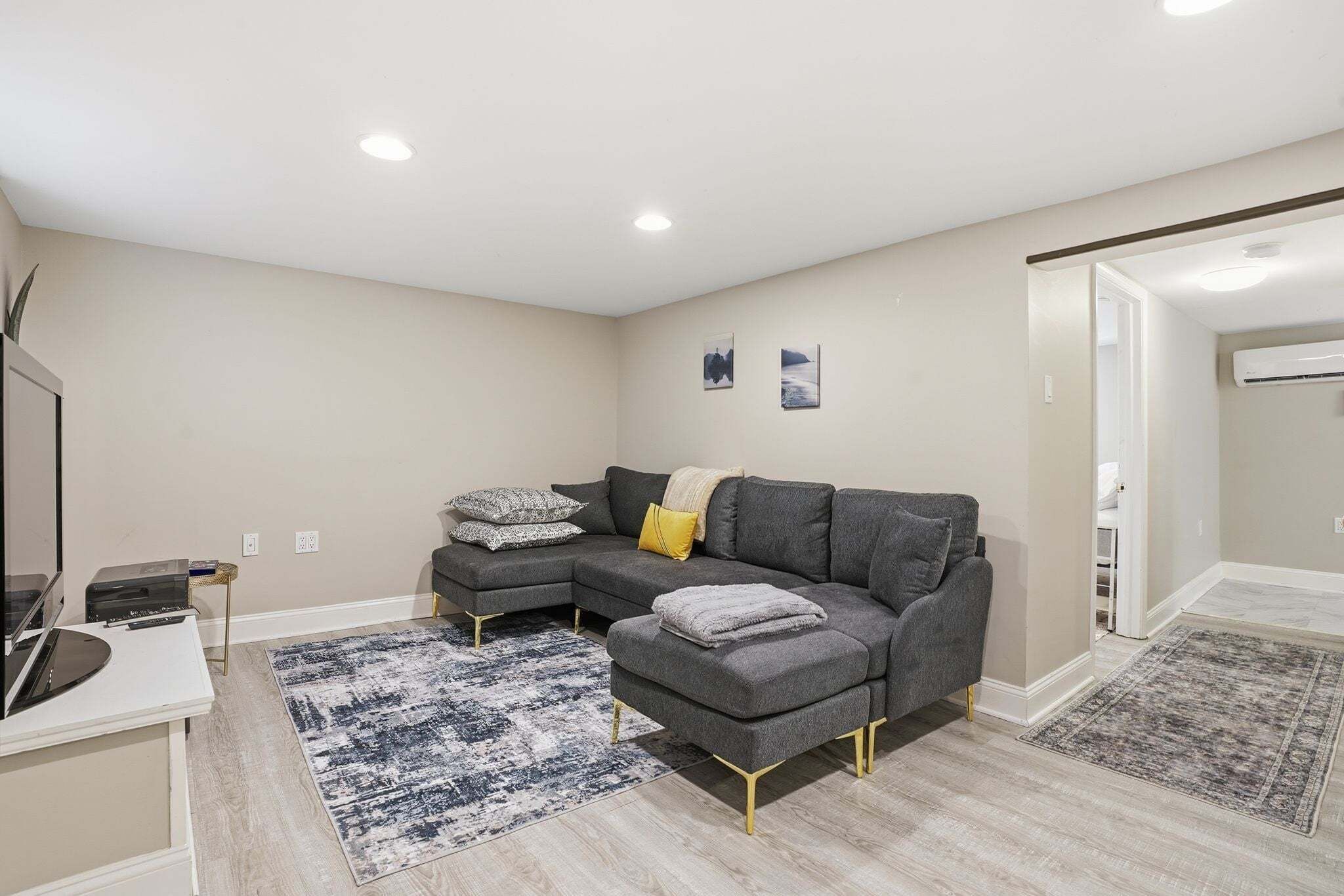 A modern living room with a grey sectional sofa, a small white desk, and two rugs.