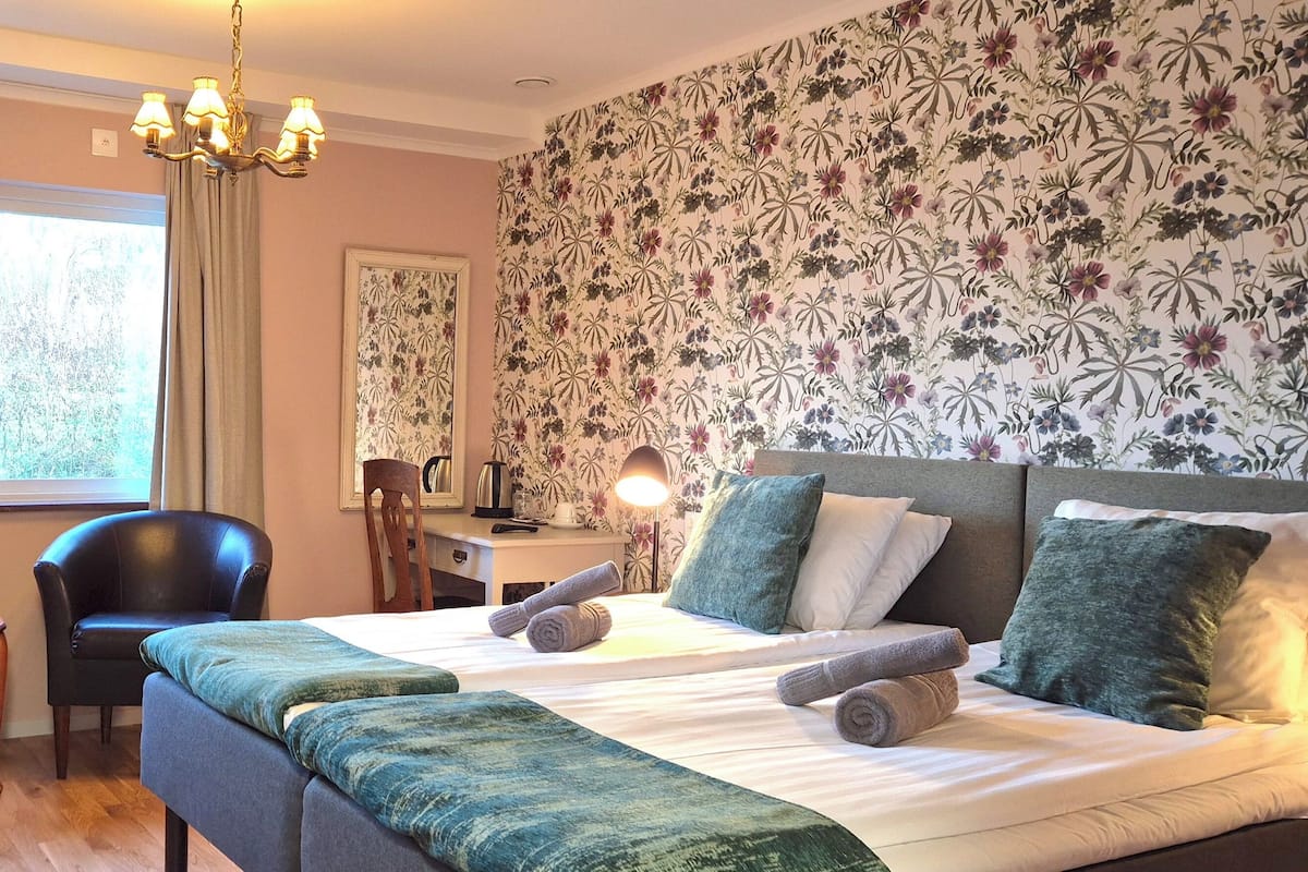 A hotel room with a bed, two chairs, a desk, and a chandelier.