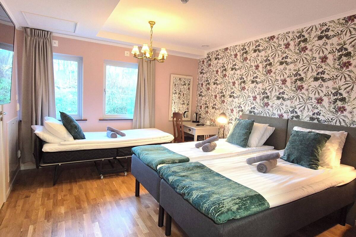 A hotel room with two beds, a desk, a chair, a TV, and a window.