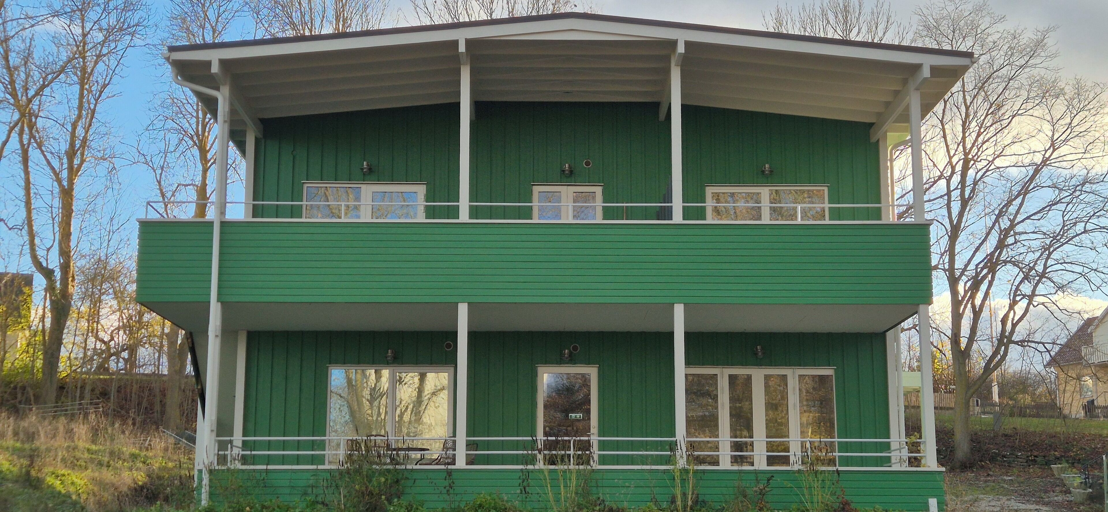 A two-story building with a green exterior and white trim. It has multiple windows and a balcony on the upper floor.