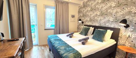 Un dormitorio con cama, escritorio, silla, ventana y pared con papel tapiz floral.