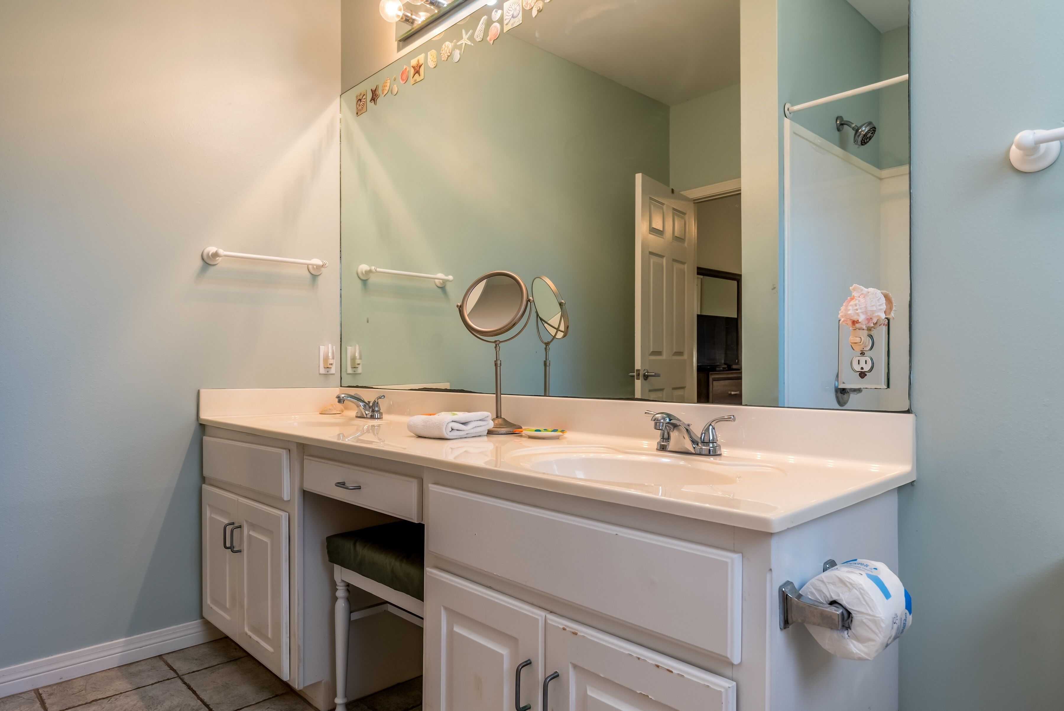 A bathroom with two sinks, a mirror, a towel rack, and a toilet paper holder.
