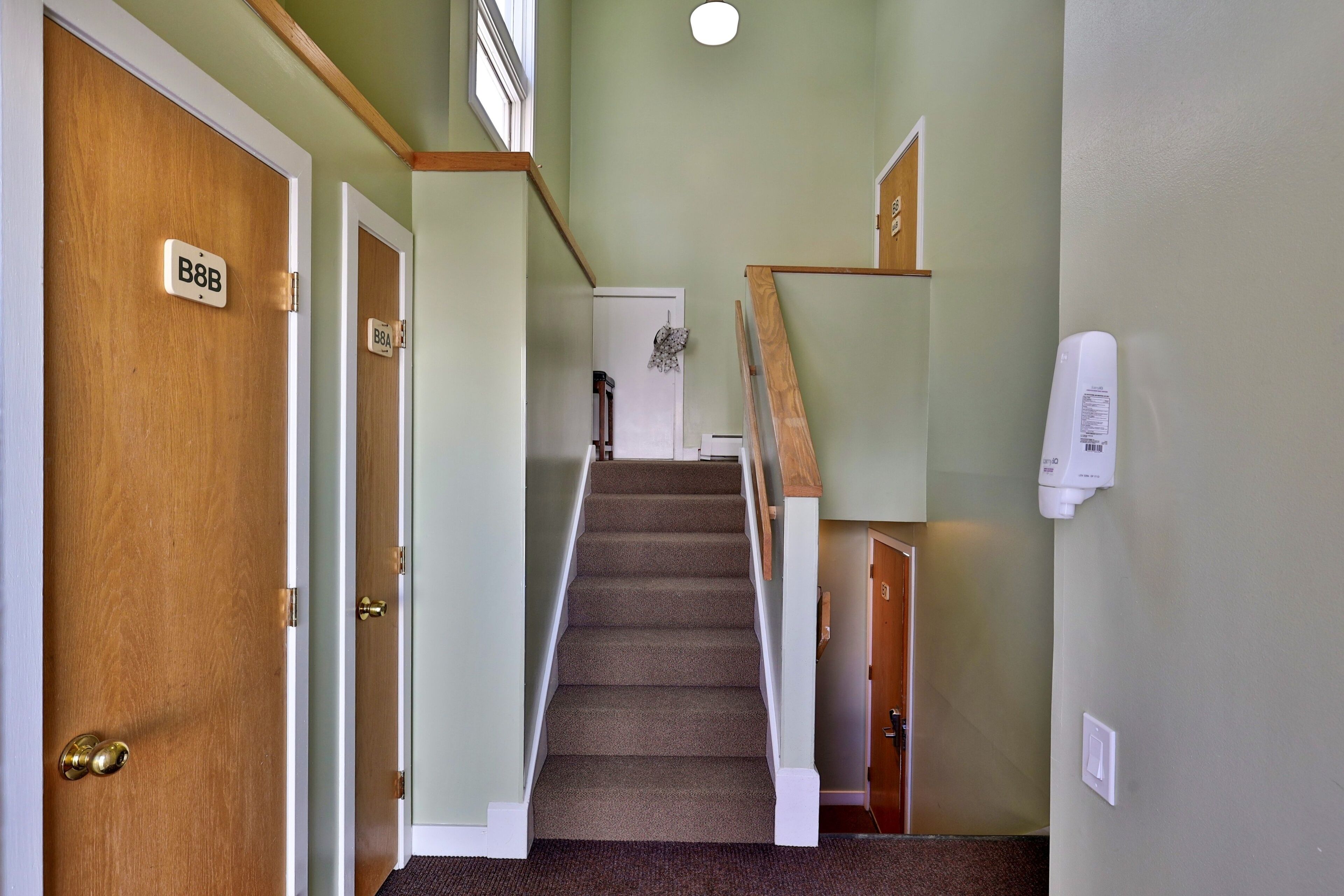 A carpeted staircase with wooden handrails and a white wall with a smoke detector.