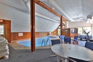 Una piscina interna con vista sull'esterno, circondata da sdraio e attrezzature per esercizi.